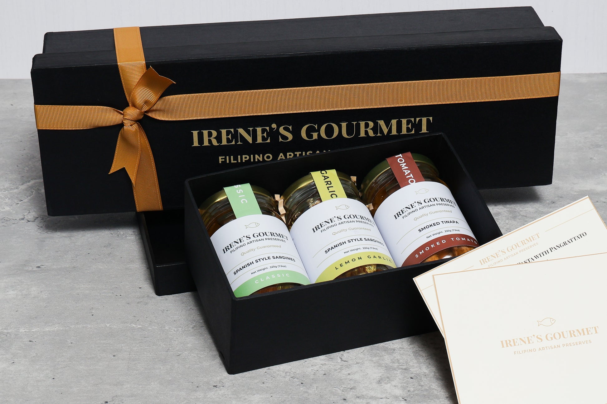 Gift box from Irene's Gourmet with jars of food and a card on a gray surface