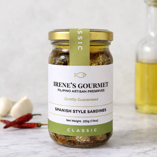 Jar of Irene's Gourmet Spanish Style Sardines on a marble surface with garlic and chilies in the background.