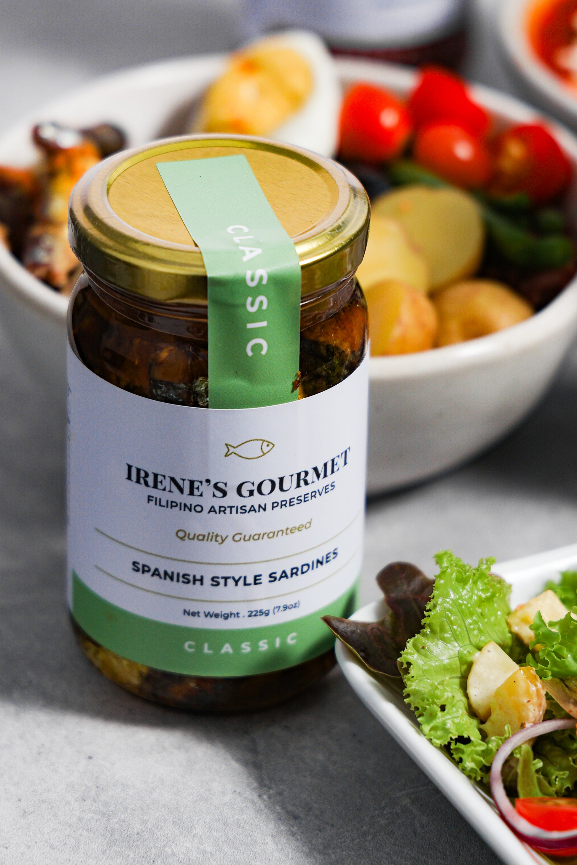 Jar of Irene's Gourmet Spanish Style Sardine with a salad and other dishes in the background
